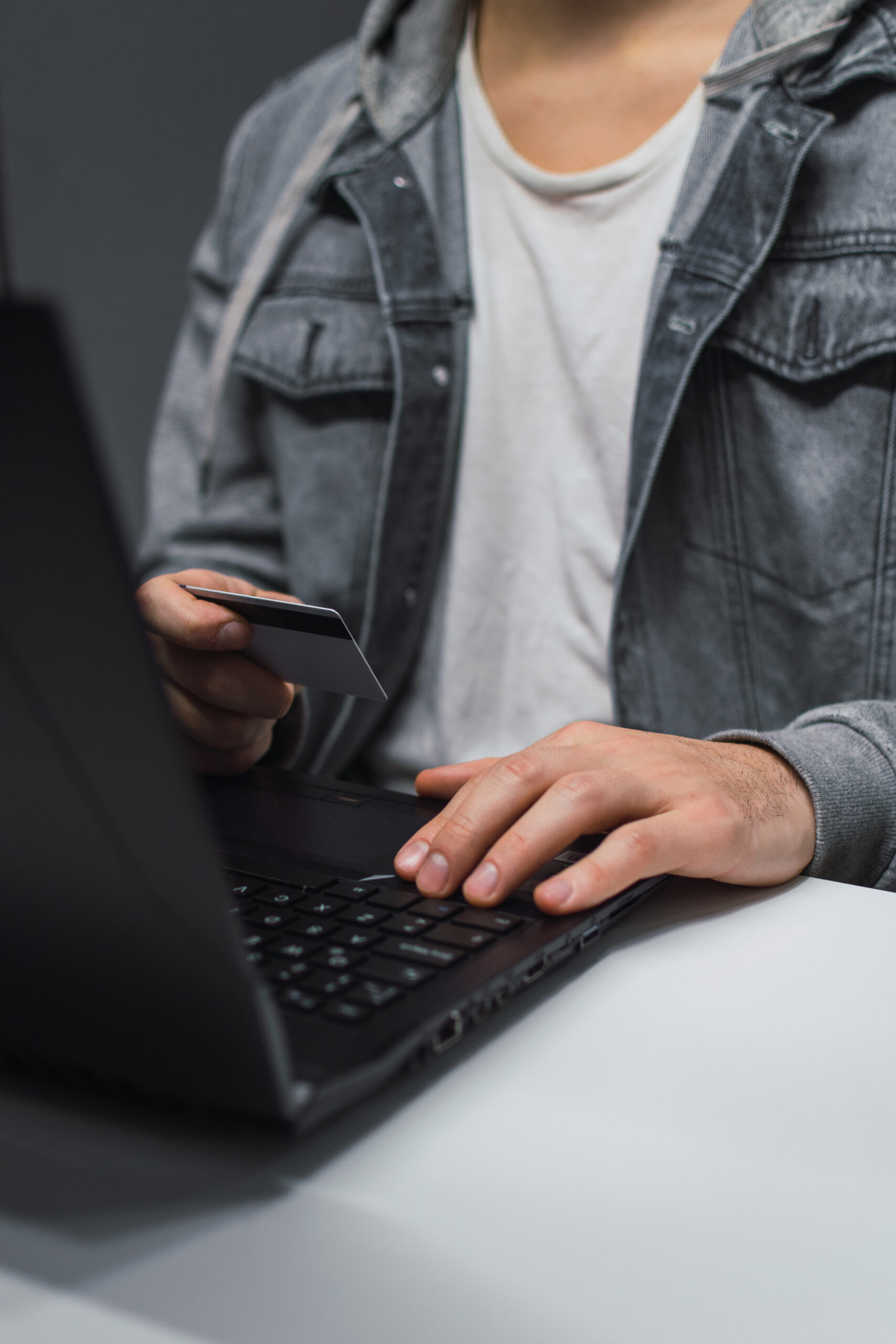 A vertical shot of a guy with his laptop and credit card making a payment online