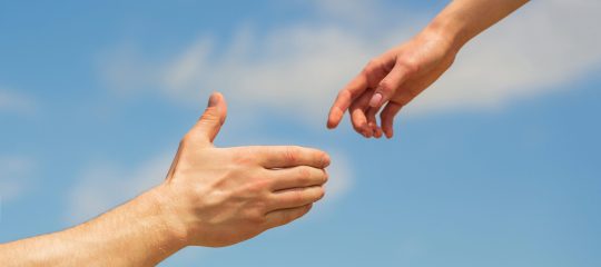 Giving a helping hand. Hands of man and woman on blue sky background. Lending a helping hand. Solidarity, compassion, and charity, rescue. Hands of man and woman reaching to each other, support.